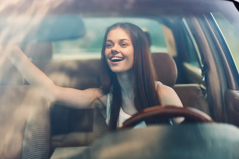 Happy young woman driving car, enjoying the road trip experience with sunlight filtering through the windshield, capturing joy and freedom.