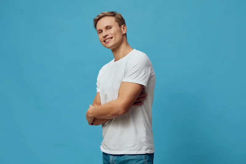 Smiling man standing crossed arms white t-shirt casual wear blue background studio portrait digital nomad concept