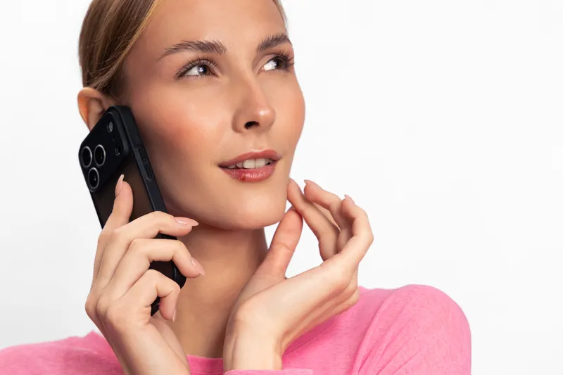 Young woman in pink sweater talking on smartphone with thoughtful expression. Isolated on white background. Concept for communication, technology, and modern lifestyle.