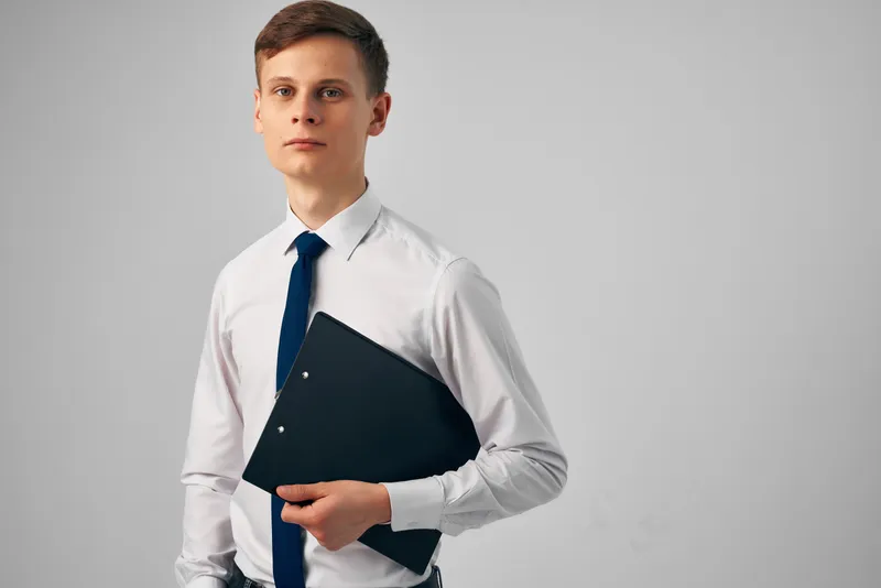 Менеджер в белой рубашке с галстуком, с черной папкой и документами, позирует для фото