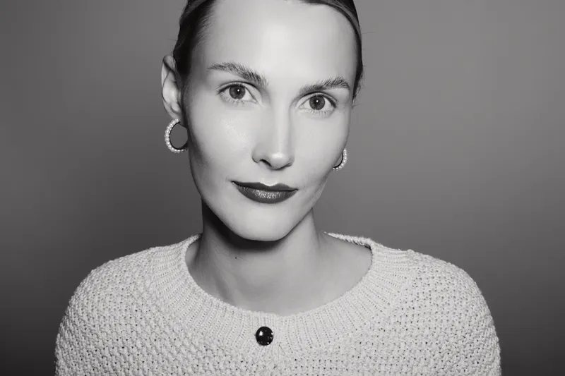 Close-up portrait of a young Caucasian woman with fair skin wearing a knitted sweater and hoop earrings. Studio lighting highlights her natural beauty and elegant expression.
