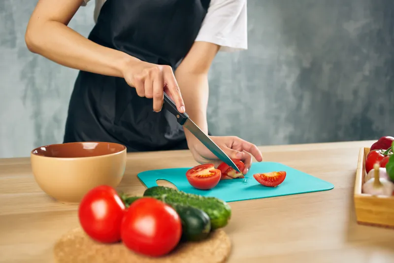 Женщина в черном фартуке на кухне нарезает овощи для салата, придерживаясь диеты