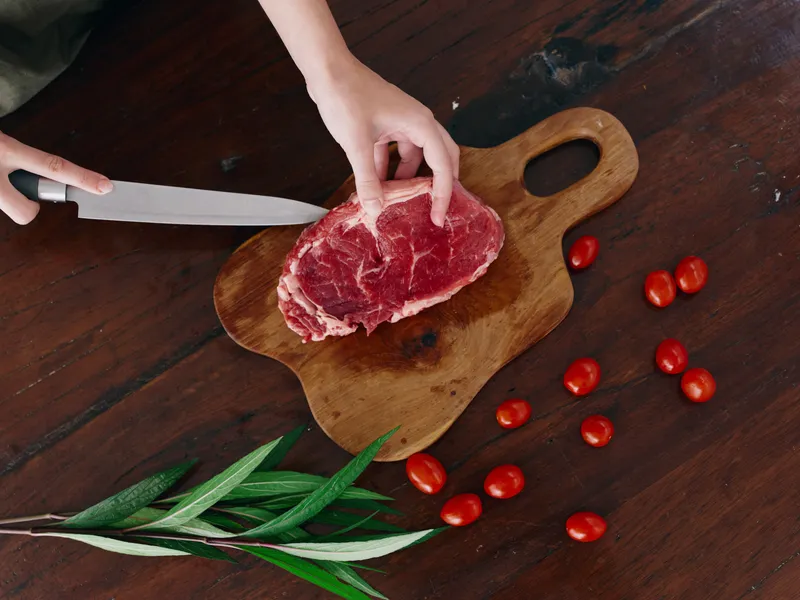 Женщина с ножом в руке нарезает свежее мясо стейка для жарки на кухне