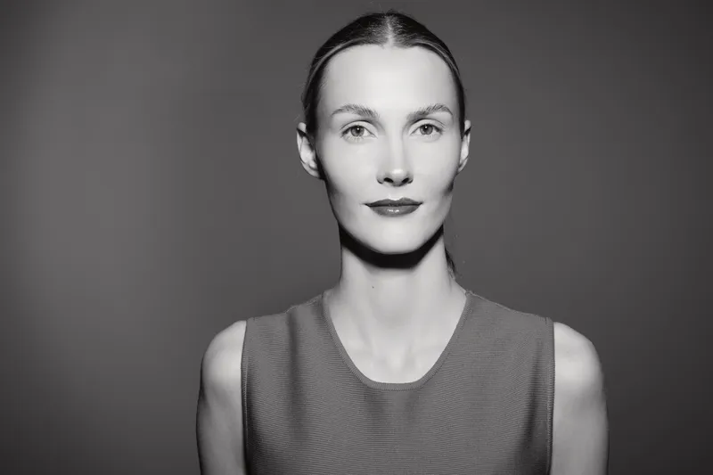 Portrait of a fair skinned Caucasian woman with slicked back hair wearing a sleeveless top against a dark background. Concept of minimalism and beauty.