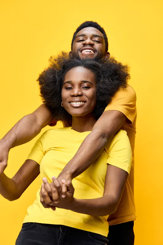Happy African couple embracing each other in matching yellow outfits against a vibrant yellow background, showcasing love and joy in a seasonal, cheerful atmosphere