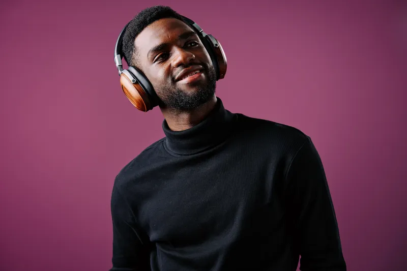 Young Black man wearing headphones and smiling against a vibrant purple background, showcasing modern style and positive emotions