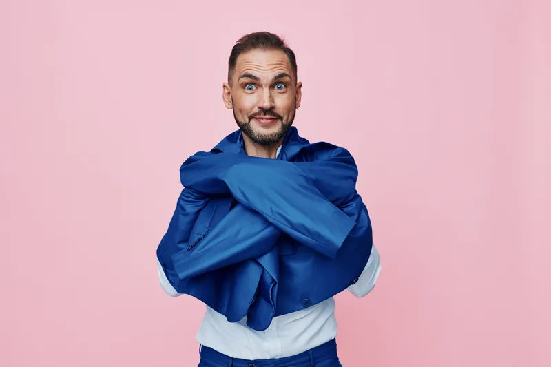 A professional man in business attire stands against a solid pink background, exuding confidence and energetic mood with arms crossed and a relaxed, friendly smile.