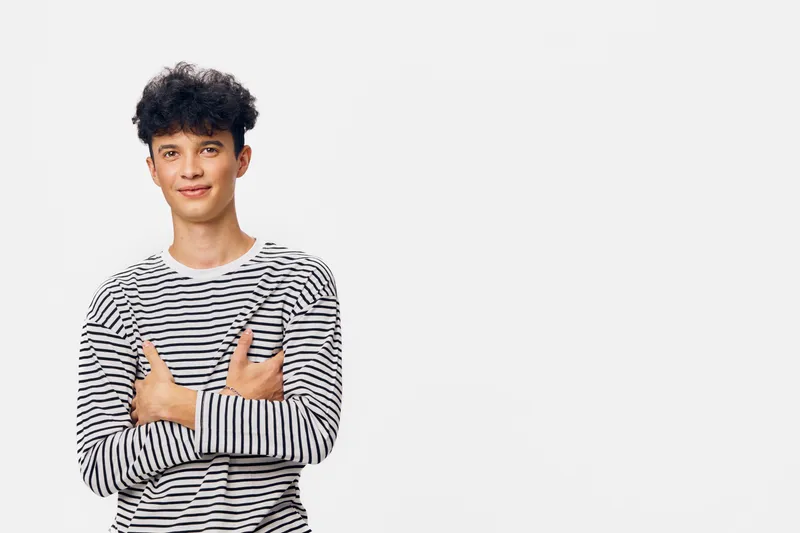 young man smiling confidently with arms crossed wearing a striped sweater against a white background, casual style and positive mood