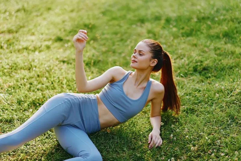 Fit young woman in activewear relaxing on grass, showcasing a healthy lifestyle, summer vibe, and tranquility in nature