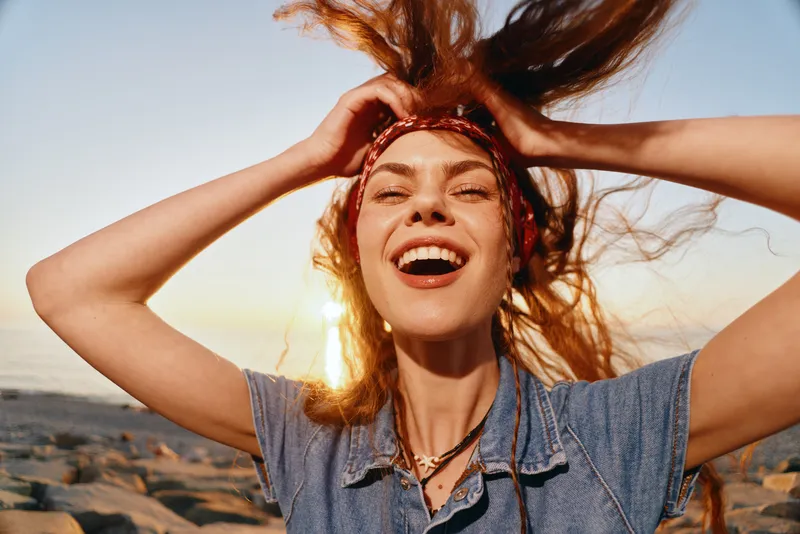 Lifestyle woman smiling joyfully in modern boho-western denim street style with film color effect, bright outdoor natural light and casual accessories.