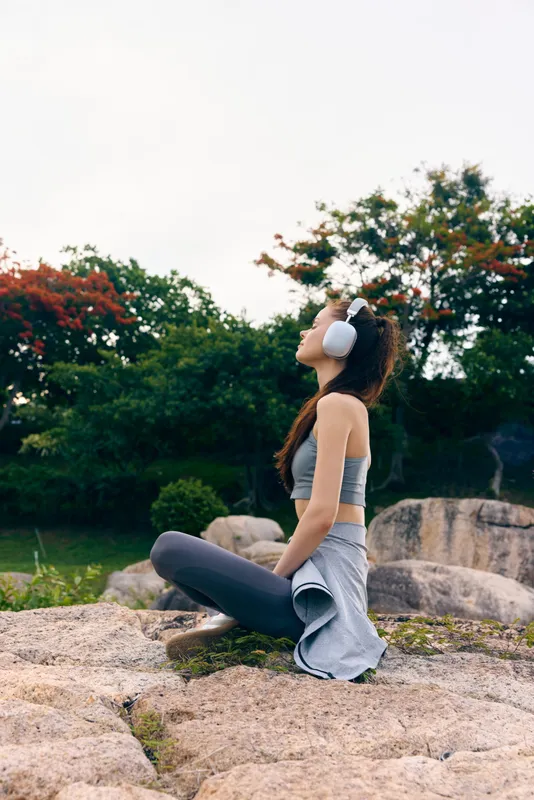 A young woman practicing yoga outdoors, wearing a sporty outfit and headphones, immersed in relaxation amidst nature s greenery and colorful foliage