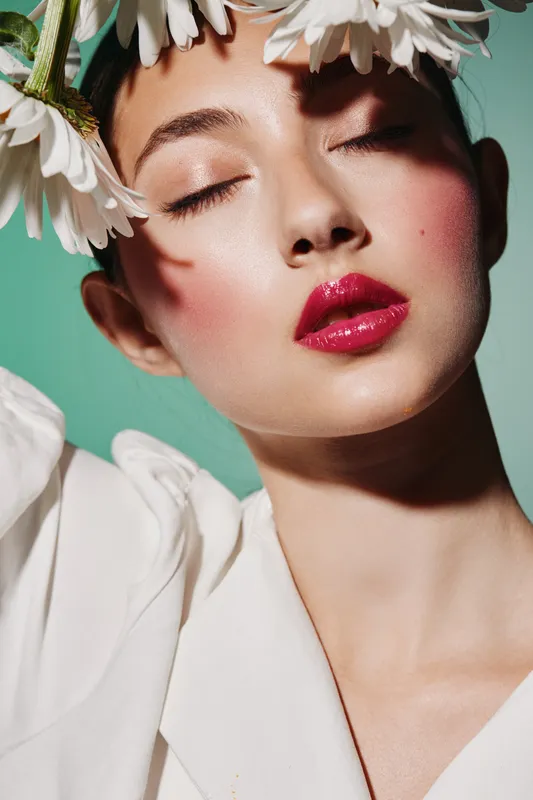 Close-up of a woman with glossy red lips and soft skin wearing a white outfit surrounded by white flowers. Concept for beauty, fashion, creative, and skincare photography.