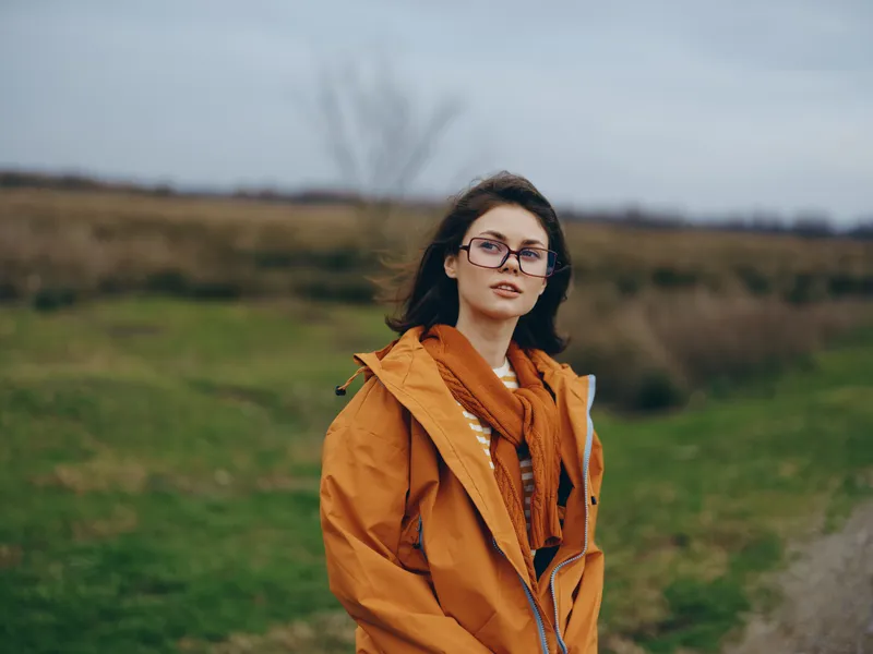 Woman, lifestyle, outdoors, portrait, autumn, jacket, scarf, glasses, nature, countryside, standing on a road, soft cloudy light, calm smile, casual fashion, fall travel