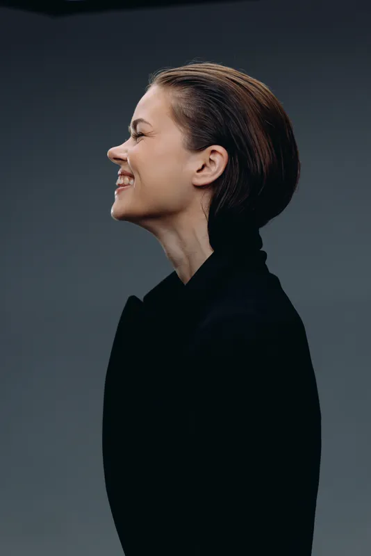 Smiling woman in black turtleneck with short hair expressing happiness and joy in studio setting.