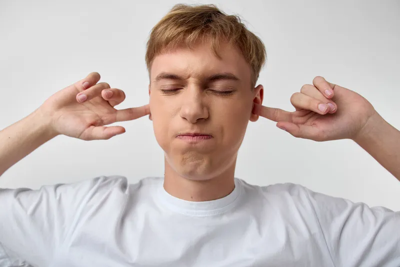 Ears covered for silence and concentration, a calm gesture with closed eyes in a simple studio, illustrating noise reduction and focus in daily life