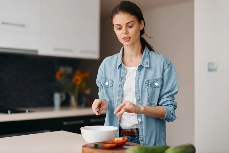 Красивая женщина стоит в уютной домашней кухне и готовит вкусный здоровый салат из свежих овощей