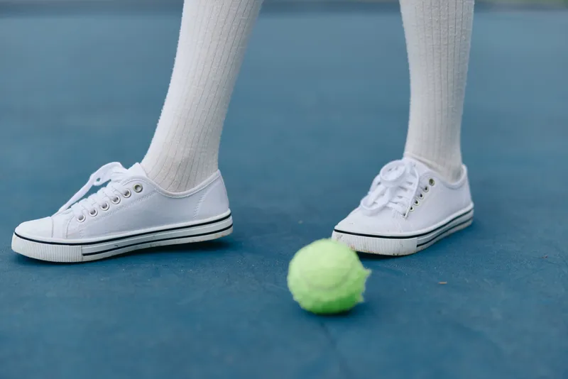 Close up of white sneakers on a tennis court with a green tennis ball, capturing a sporty vibe and seasonal outdoor activity