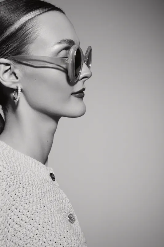 Profile of a fair skinned Caucasian woman wearing round sunglasses and textured sweater. Studio portrait with soft lighting on a plain background. Concept for fashion and style.