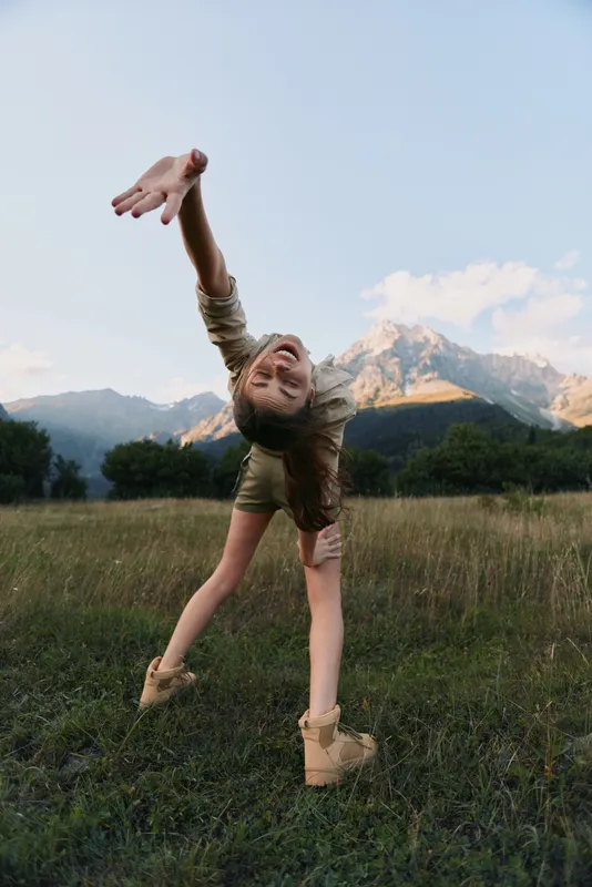 Woman dancing in a grassy field with distant mountains, conveying joyful movement and a carefree lifestyle in an outdoor scene.