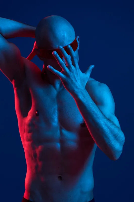 Athletic man posing in a dynamic blue and red light, showcasing strength and confidence with a stylish touch. This striking image conveys a sense of modern artistry.