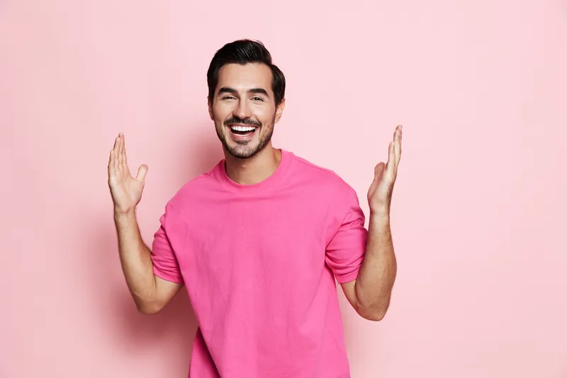 Full body smiling cheerful young man wearing pink sweater looking at the camera with hands raised, isolated on solid pink background. Positive lifestyle concept.
