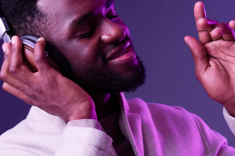 Young Black man enjoying music with headphones, expressing joy and relaxation against a vibrant purple background