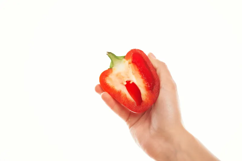 Женщина держит в руках красный перец, готовя овощи на кухне