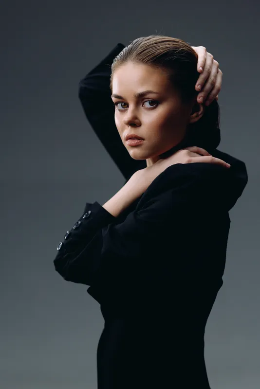 serious woman in black dress posing with hand on head with dark background