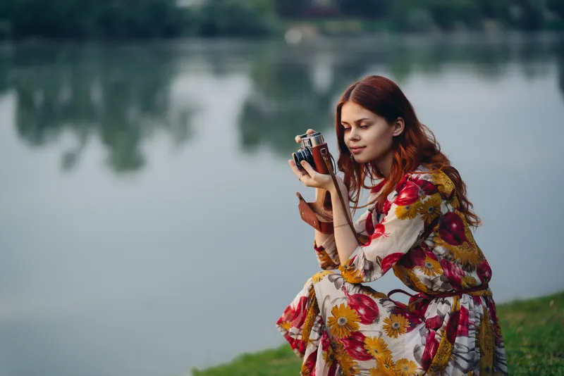 Симпатичная женщина с фотоаппаратом у озера на отдыхе на природе