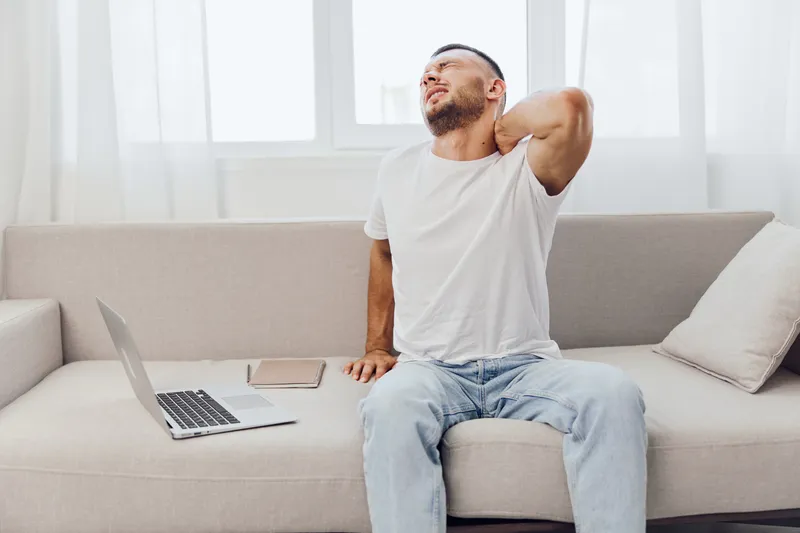 A man experiencing discomfort while working from home, surrounded by technology, highlighting the challenges of work-life blur, mental health, and emotional minimalism.