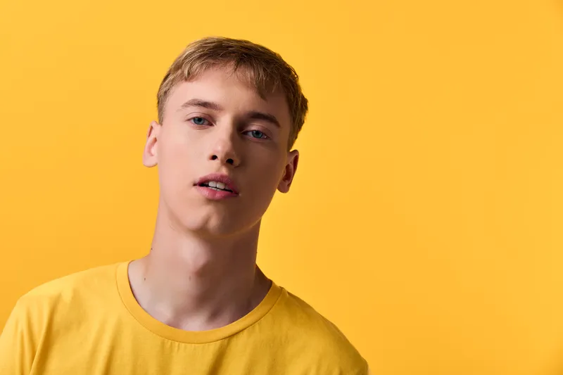 Young man yellow tshirt in studio lighting; minimalist monochrome setting; fashion model in a headshot style with bold color; studio setup and soft shadows create a modern casual wear vibe