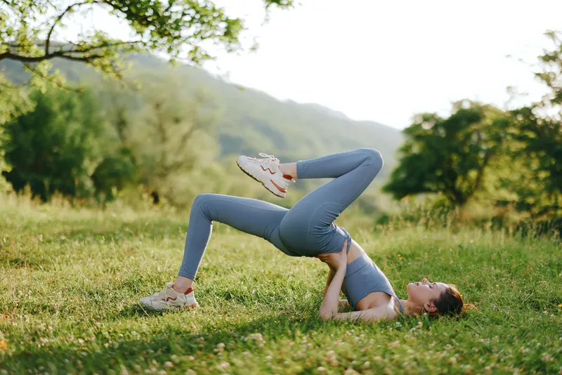 Young woman practicing yoga outdoors in a serene green landscape, showcasing strength and flexibility in a peaceful, reflective moment