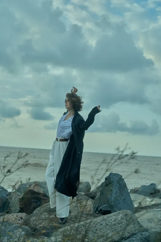 Windy sea, flowing dress on a rocky shore as a woman faces the horizon, captured by ocean breeze and dramatic clouds, maritime mood and free spirit in motion