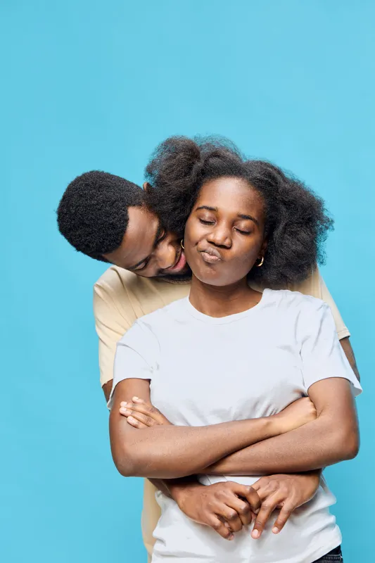 Young happy couple embracing against a pastel blue background, showcasing love and connection with joyful expressions and casual clothing