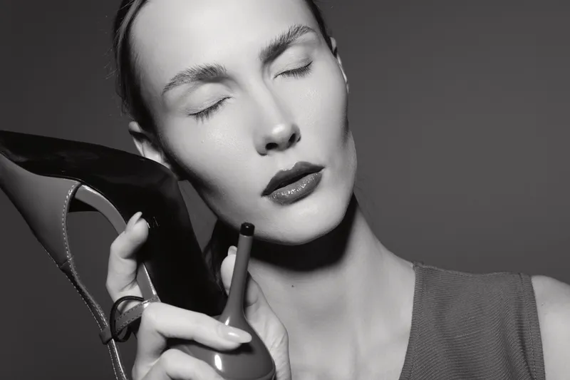 Portrait of a fair skinned white woman with closed eyes holding a high heel shoe near her face in a monochrome studio. Concept for fashion, beauty, and emotion.