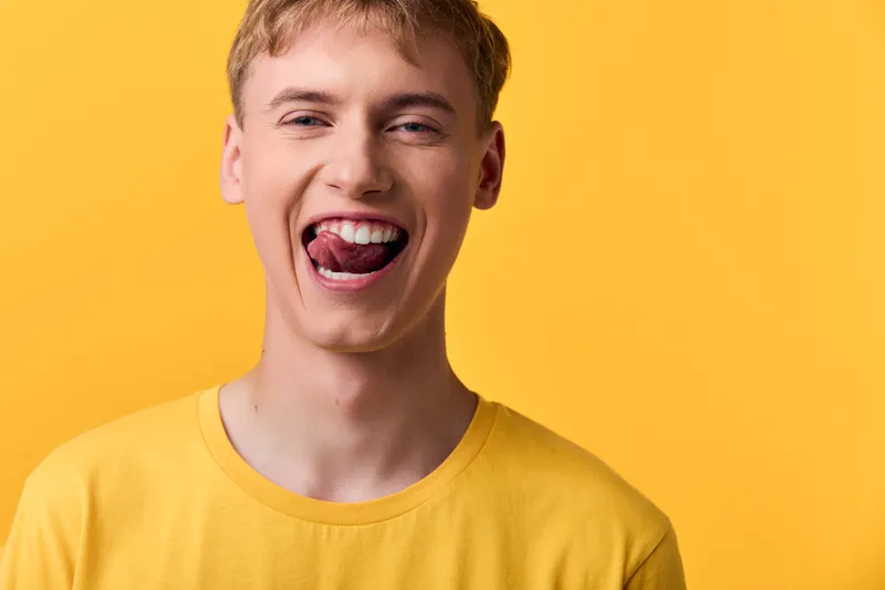 Playful, yellow clad youth with a tongue out smile in a bright studio, conveying bold fashion and energetic mood, ideal for lifestyle, humor, and youthful expression in creative campaigns