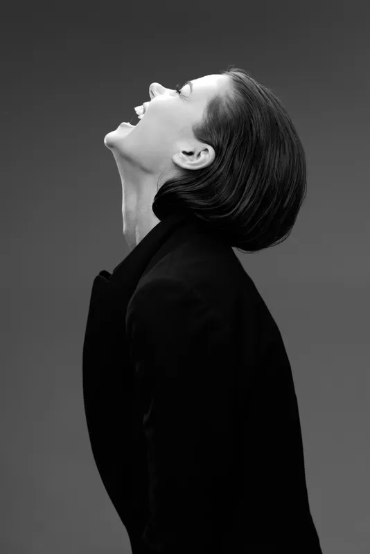 Black and white portrait of a smiling woman in a black outfit expressing joy and confidence with a dark background.