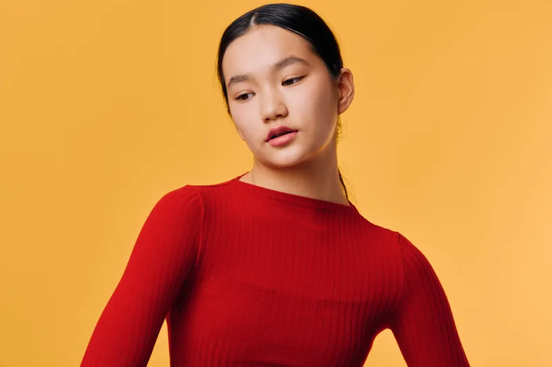 Portrait of young woman in red sweater looking sideways on yellow background with serious emotion, studio shot with clean minimal style and modern fashion concept.