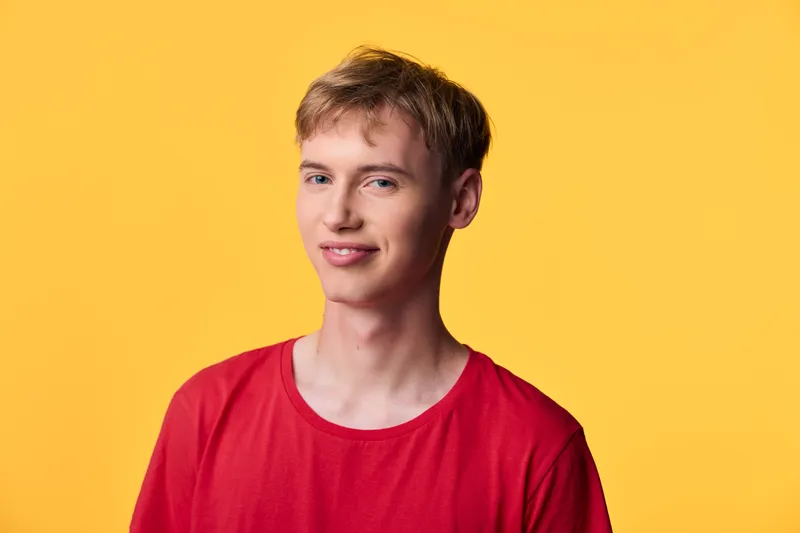 Young man with a bright, cheerful smile wearing a red shirt stands before a yellow background, creating a casual headshot suitable for fashion and lifestyle branding