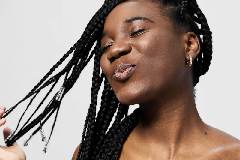 Happy young woman with braided hair, smiling and enjoying her hairstyle in a bright, minimalistic background, showcasing confidence and joy