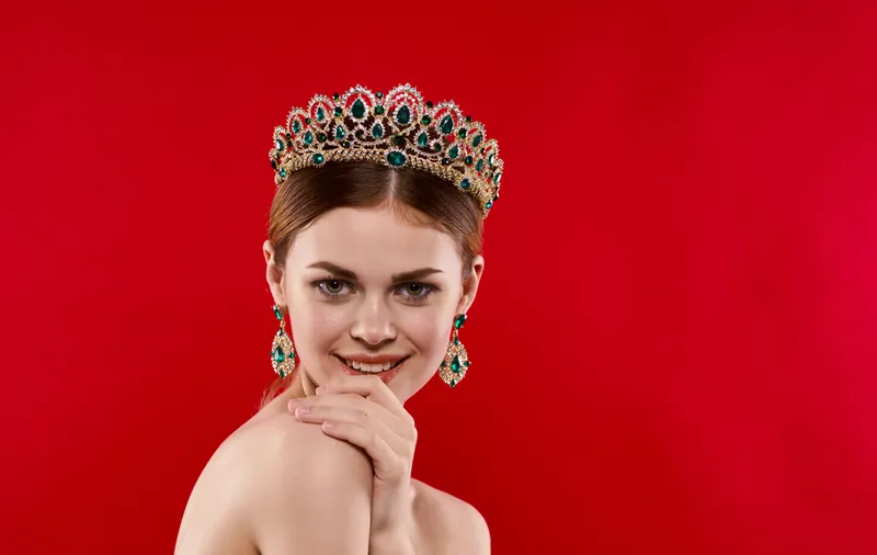 Портрет уверенной женщины на красном фоне с короной на голове и серьгами в ушах