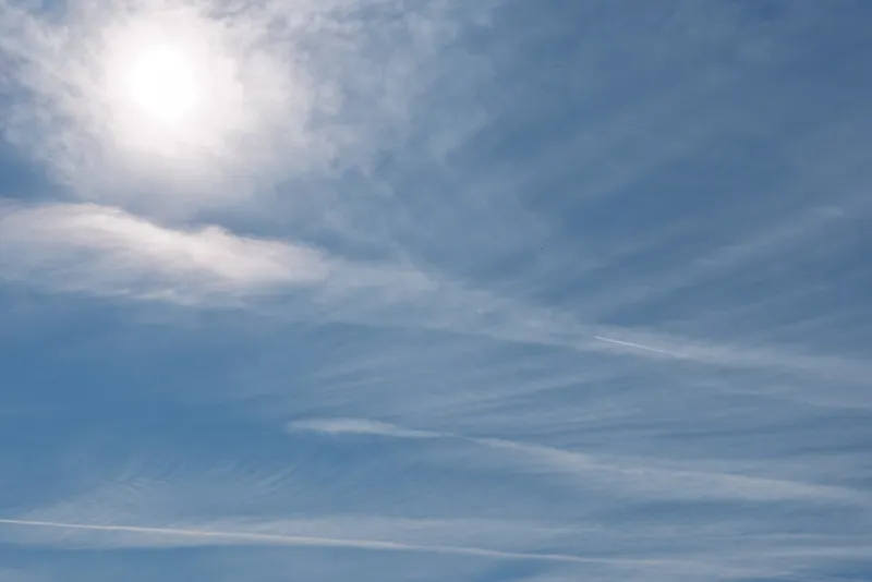 Clear blue sky with wispy cirrus clouds and a bright sun in the upper left, creating a calm outdoor atmosphere and spacious feel for travel, nature, or weather themed projects