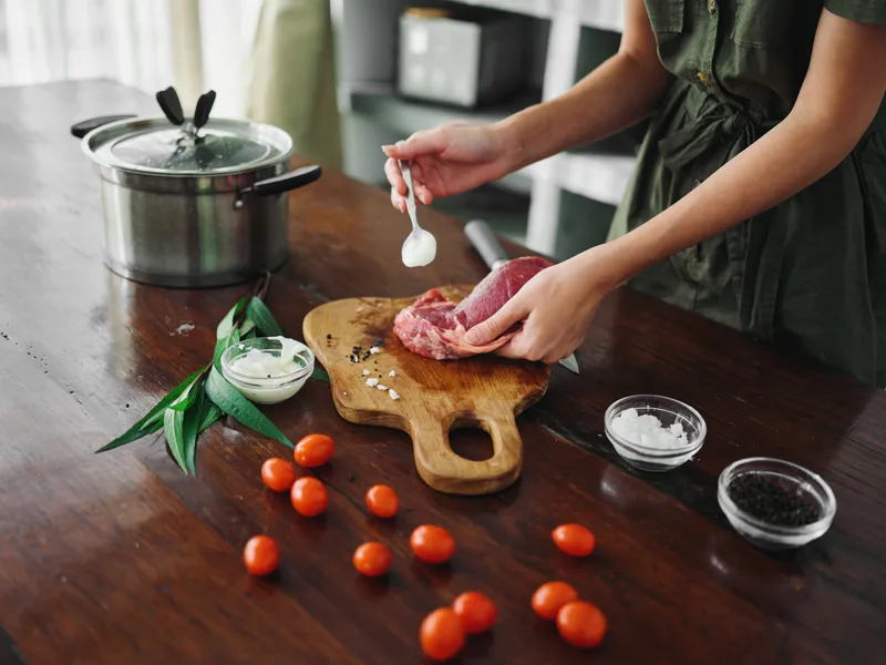 Женщина на кухне готовит ужин из мяса, овощей и специй на деревянном столе на фоне стильной кухни, крупный план рук, свежие экопродукты, образ жизни