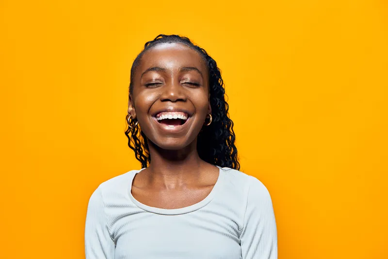 Cheerful young girl with curly hair smiling against a vibrant yellow background, exuding joy and positivity in a casual outfit