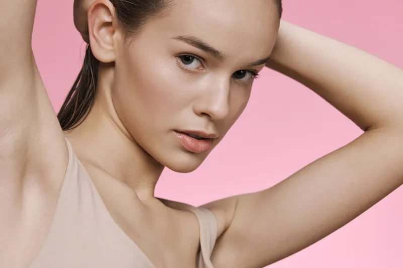 Confident young woman with neutral makeup posing against a pink background, showcasing a natural beauty concept and emphasizing skin care and self care