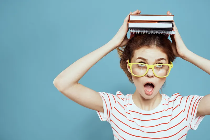 Студентка с книгами на голове и в жёлтых очках на синем фоне, обрезанный вид