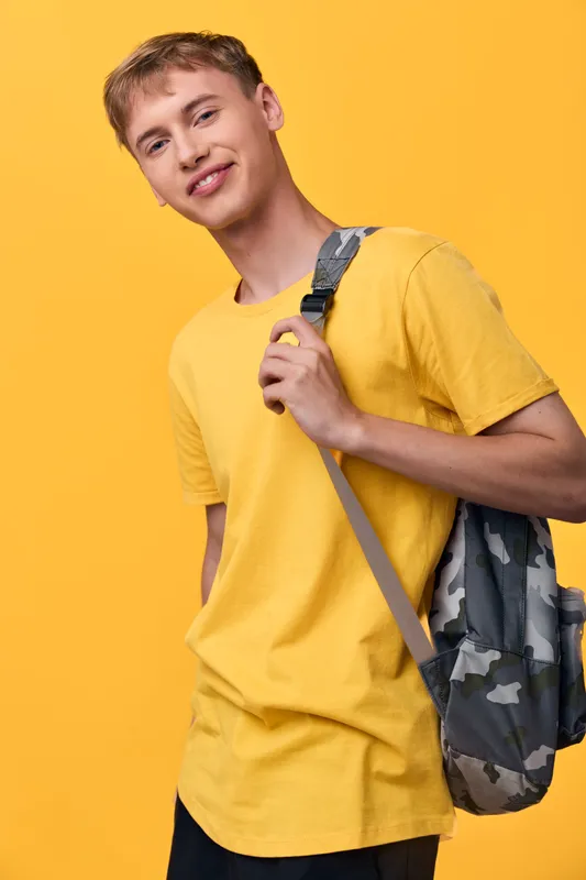 Student in a bright yellow t shirt with a camo backpack stands casually against a vivid yellow backdrop, ready for school travel and daily adventures around town