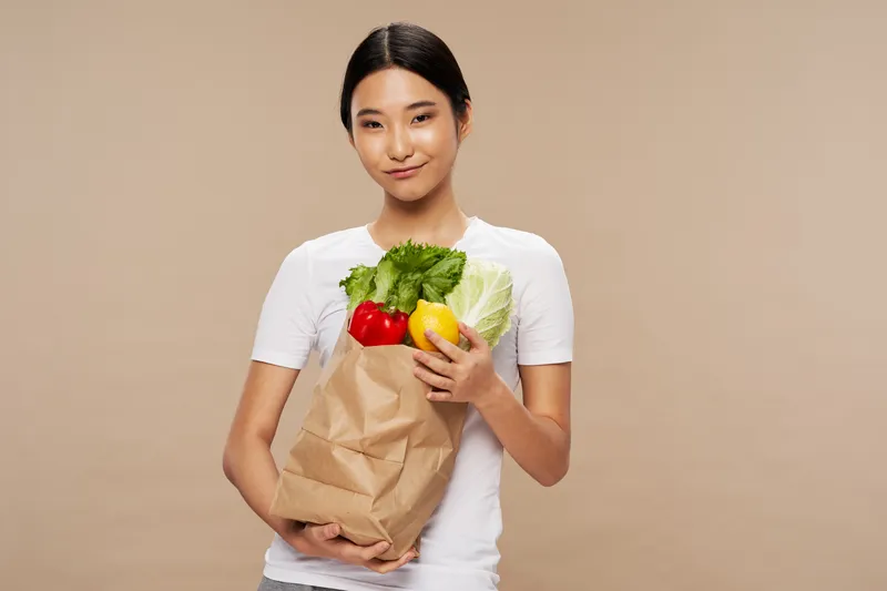 Стройная женщина с пакетом продуктов в руке на бежевом фоне, обрезанный вид, диета