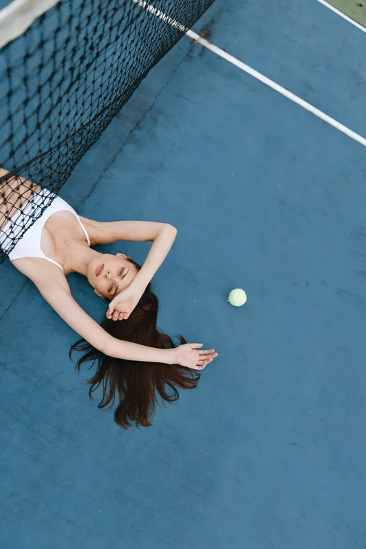 A young woman in a white sports bra relaxing on a blue tennis court, capturing a sense of leisure, summer, and the joy of sports