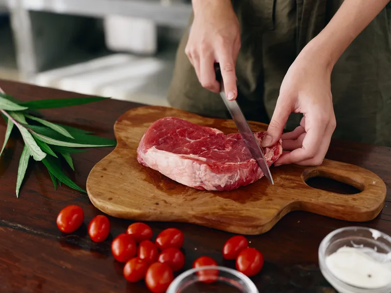 Женщина с ножом в руке нарезает свежее мясо для жарки на кухне